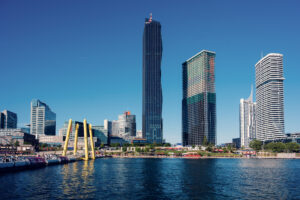 Donau City skyline and the yellow Ponte Cagrana pylons rising over the Copa Beach promenade.