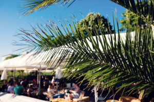 Palm fronds framing a busy Copa Beach bar terrace on a sunny afternoon.
