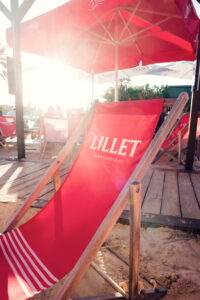 A red deck chair under a parasol on the Copa Beach sand at sunset.