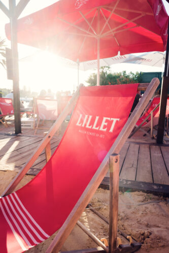 A red deck chair under a parasol on the Copa Beach sand at sunset.