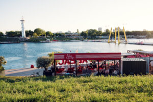 A waterfront kiosk at Copa Beach with the lighthouse and Ponte Cagrana pylons beyond.