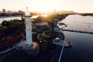 Aerial view of the white Copa Beach lighthouse and promenade at golden hour.