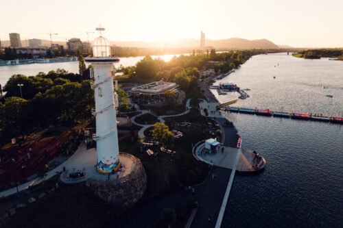 Aerial view of the white Copa Beach lighthouse and promenade at golden hour.