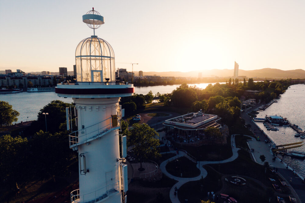 Close aerial view of the Copa Beach lighthouse lantern above the Neue Donau at sunset.