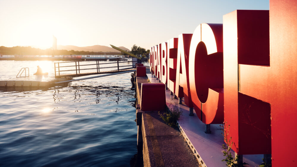 Le enormi lettere rosse COPABEACH illuminate sul molo al tramonto.
