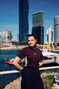 Adriana standing at the Copa Beach railing with the Donau City skyline behind her.
