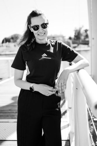 Black and white portrait of Adriana smiling in sunglasses on the Copa Beach pier.