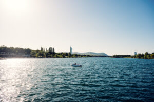 A small boat crossing the sunlit Neue Donau with the Vienna skyline in the distance.