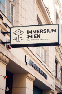 Exterior sign of Immersium Wien with geometric cube logo on the building facade.