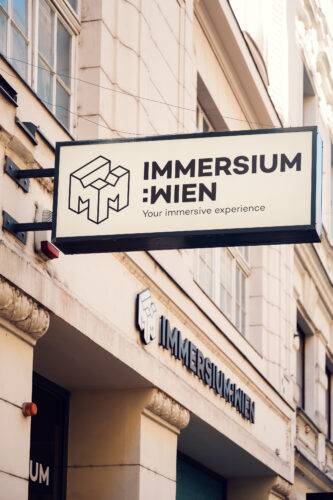 Exterior sign of Immersium Wien with geometric cube logo on the building facade.