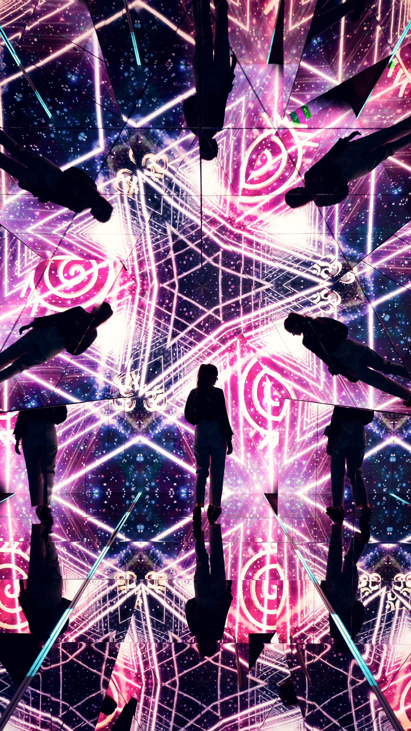 Adriana surrounded by pink and purple geometric projections inside the mirrored pyramid room.