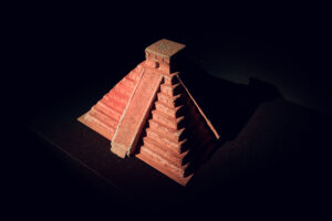 Scale model of a Maya step pyramid lit from above in a dark exhibition room.