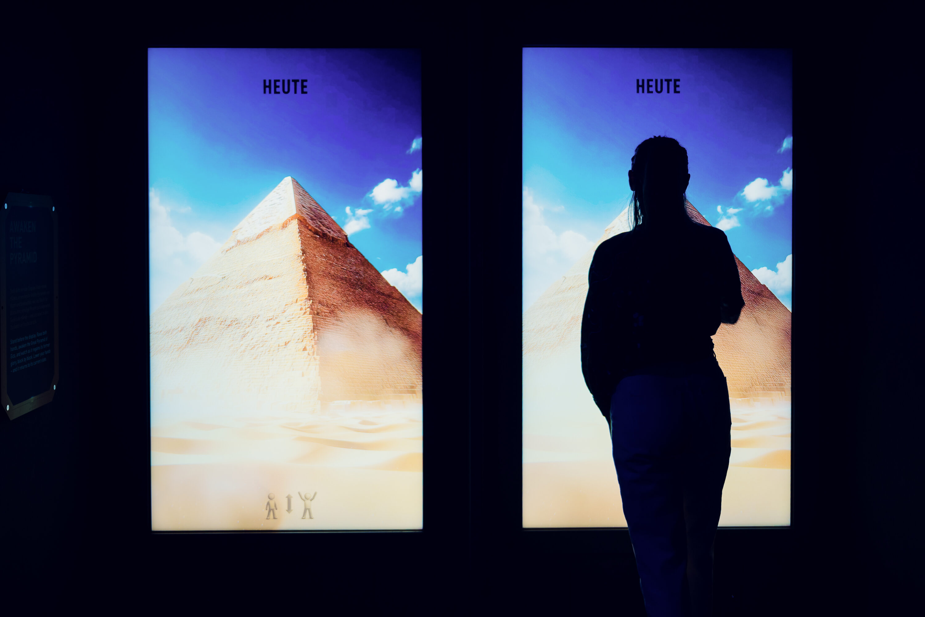 Adrianas silhouette between two backlit panels showing the pyramids of Giza labeled with the word today.