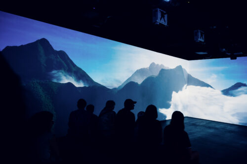 Visitors watching a mountain landscape projected across the walls of the 360-degree show room.
