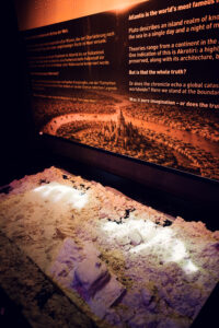 Illuminated relief model of a submerged city next to information panels about Atlantis.