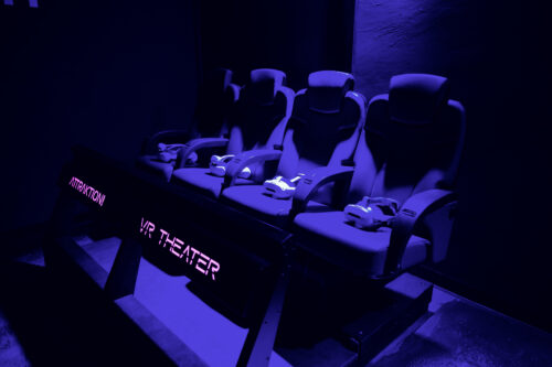 Row of motion seats with harnesses in the VR Theater lit by purple light.