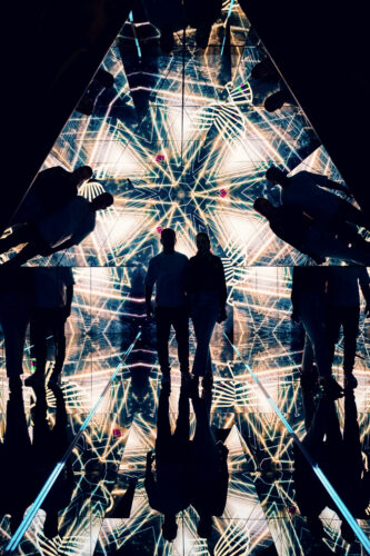 Adriana and Mario silhouette inside the mirrored pyramid room surrounded by golden geometric light patterns.