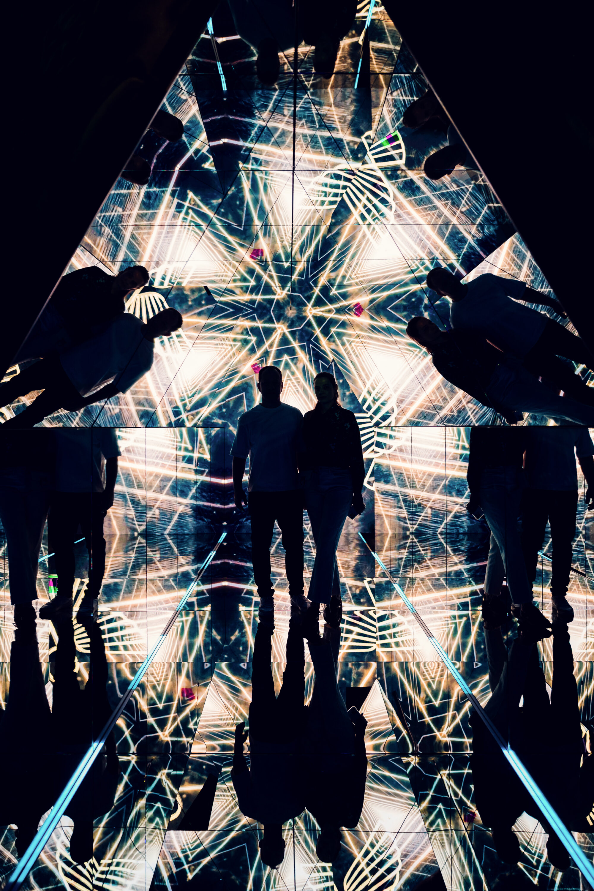 Adriana and Mario silhouette inside the mirrored pyramid room surrounded by golden geometric light patterns.