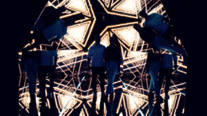Adriana and Mario standing in the pyramid room with geometric golden projections reflected around them.