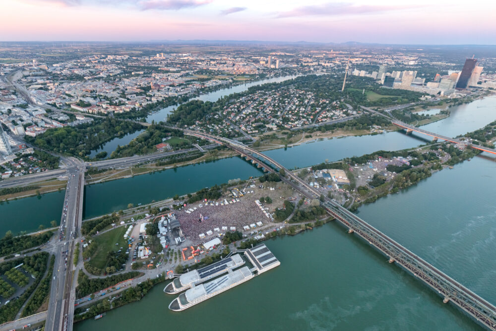 Aerial view of Donauinselfest on the Donauinsel at dusk, the festival ground between the Danube and the Neue Donau with Vienna's skyline behind © Donauinselfest / Alexander Müller