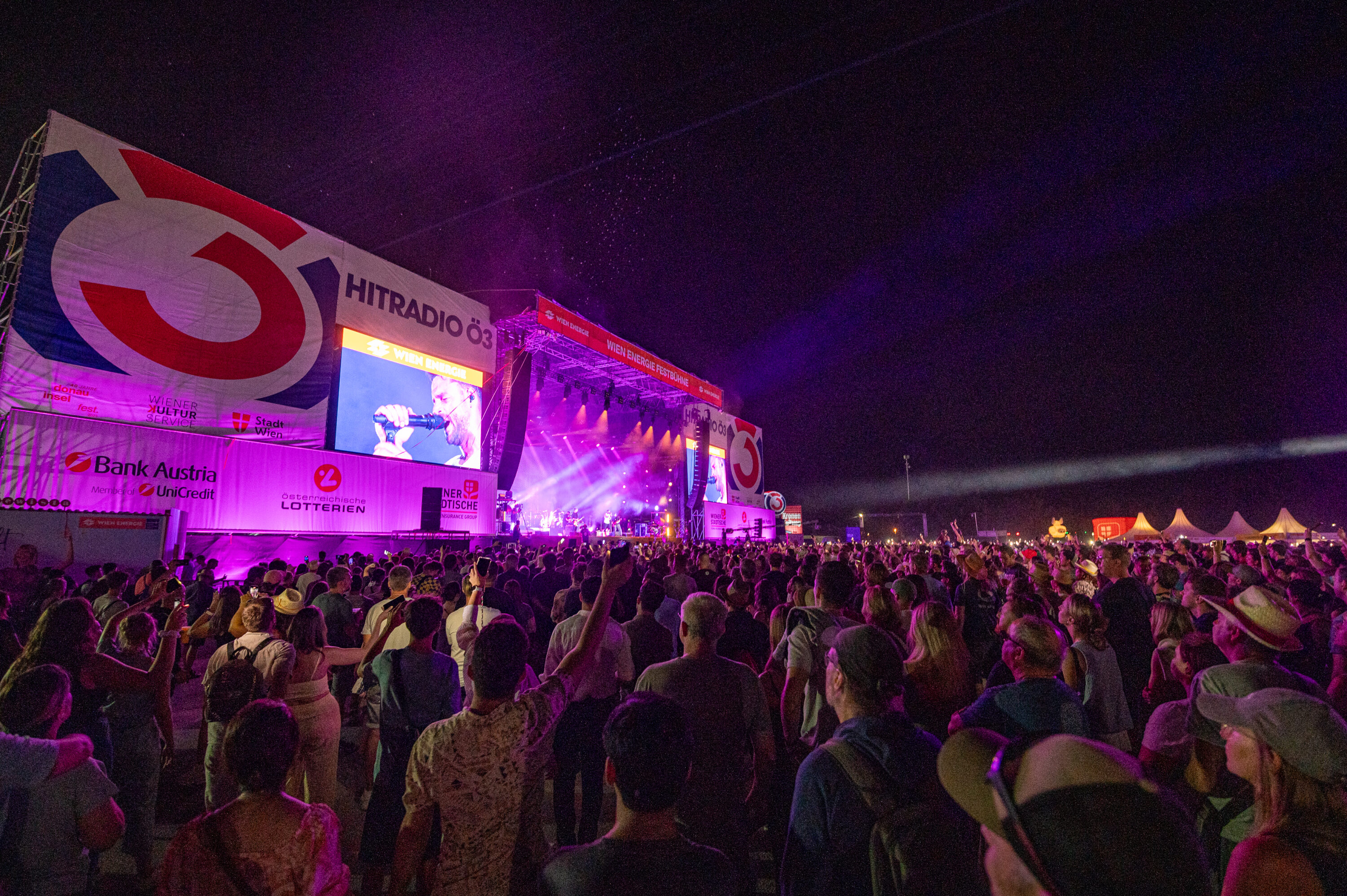Night crowd in front of the Hitradio Oe3 stage at Donauinselfest, lit purple with a performer on the big screen © Donauinselfest / Lukas Arnold