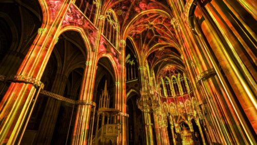 Light of Creation projections in warm gold and red across the Votivkirche nave in Vienna.
